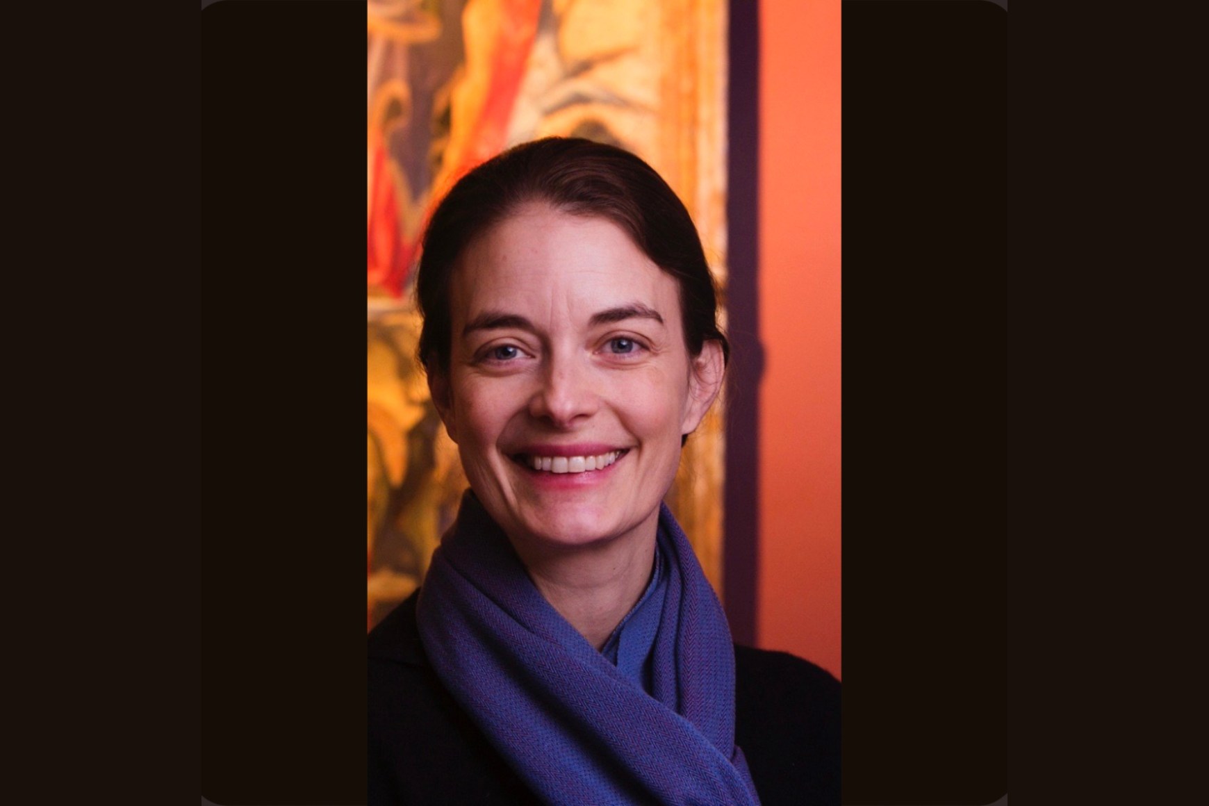 Woman in a purple scarf smiling in front of an orange background